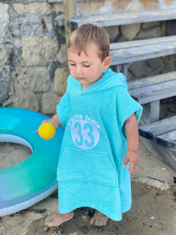 Un poncho turquoise pour bébé, estampillé "trente-trois" de la marque régionale 33.