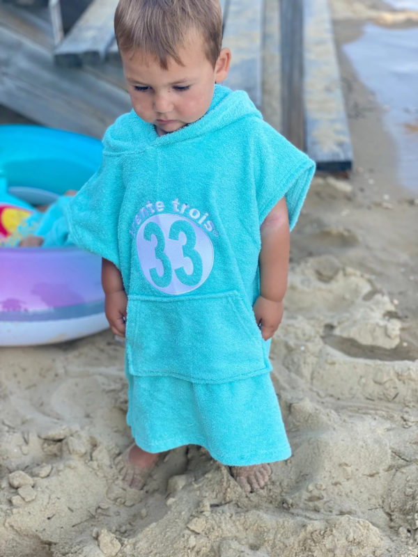 Un poncho turquoise pour bébé, estampillé "trente-trois" de la marque régionale 33.