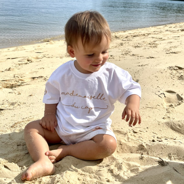 Un tee-shirt blanc pour bébé, estampillé "Mademoiselle du cap" de la marque régionale 33.