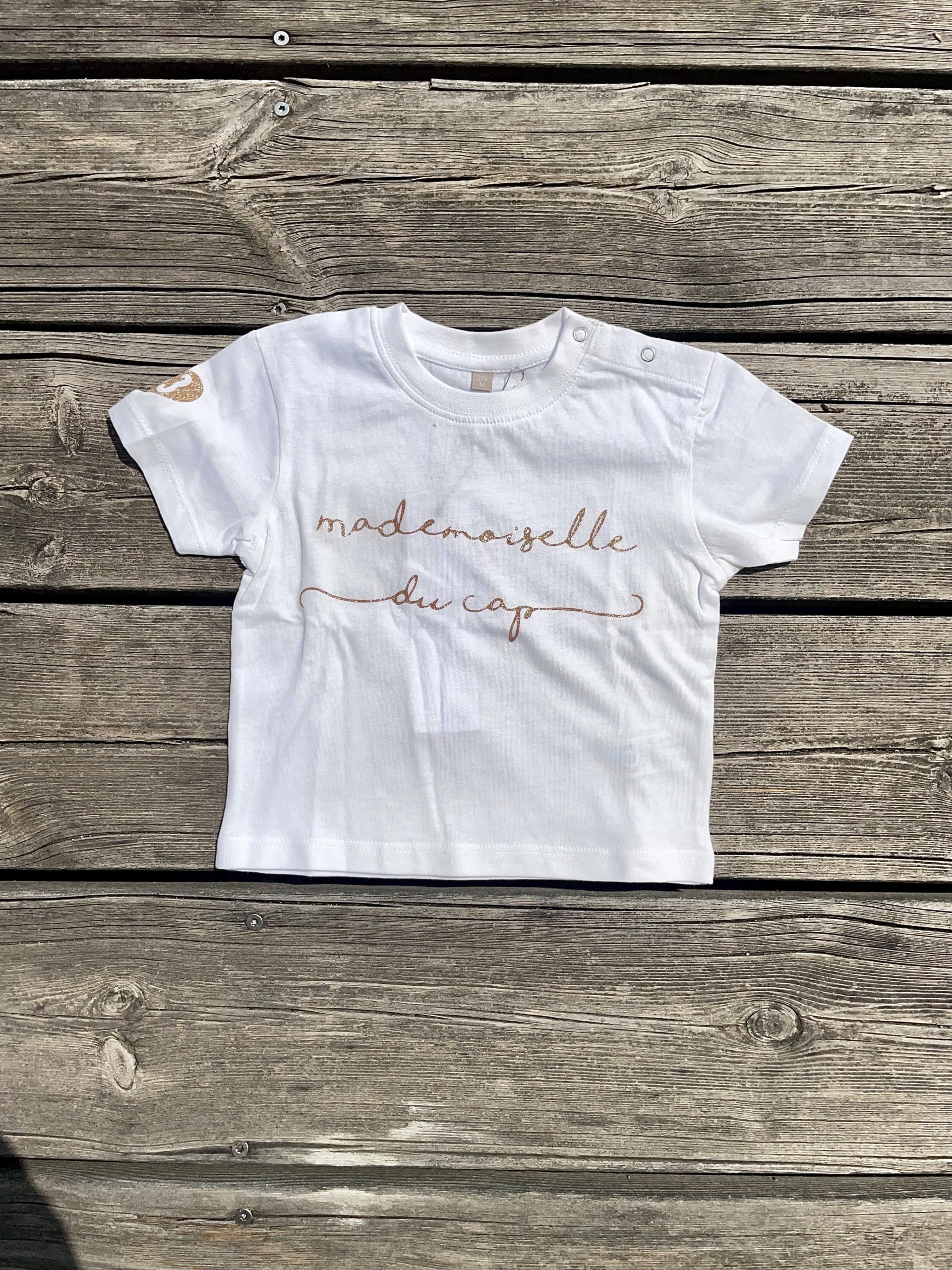 Un tee-shirt blanc pour bébé, estampillé "Mademoiselle du cap" de la marque régionale 33.